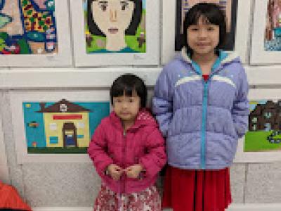Two girls stand with their artwork